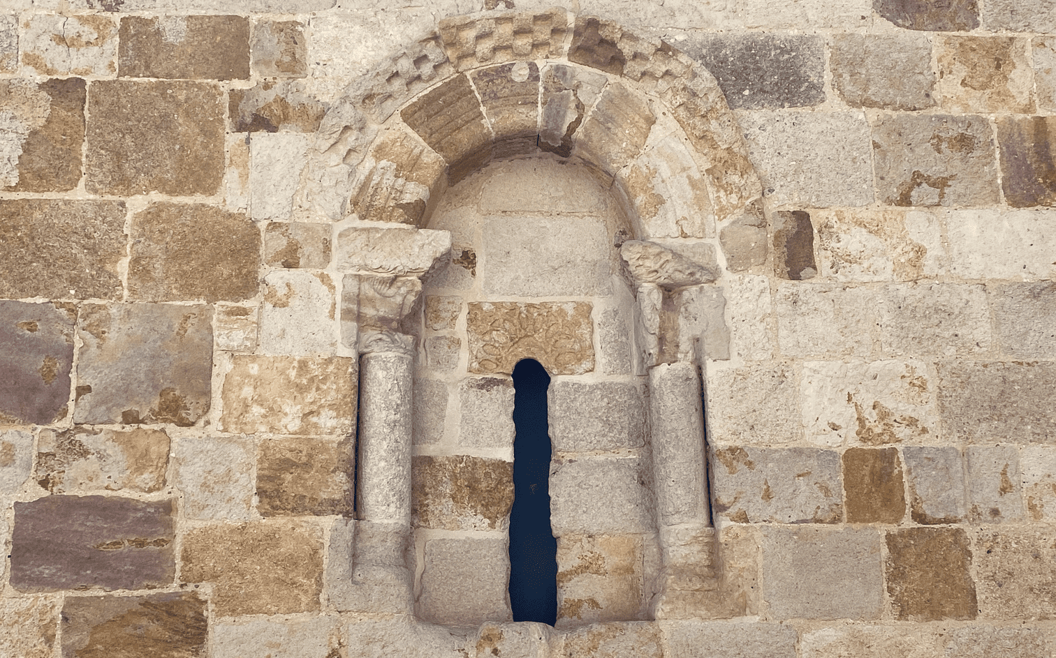 Ventana románica en aspillera, con columnillas y capiteles labrados, abierta en el muro de sillería de San Cipriano.