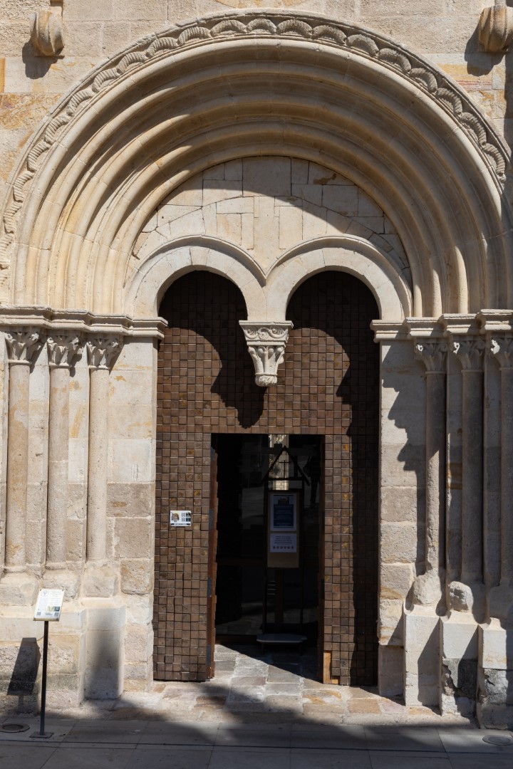 Portada románica de arquivoltas con la puerta abierta al público y un atril informativo junto a la entrada.